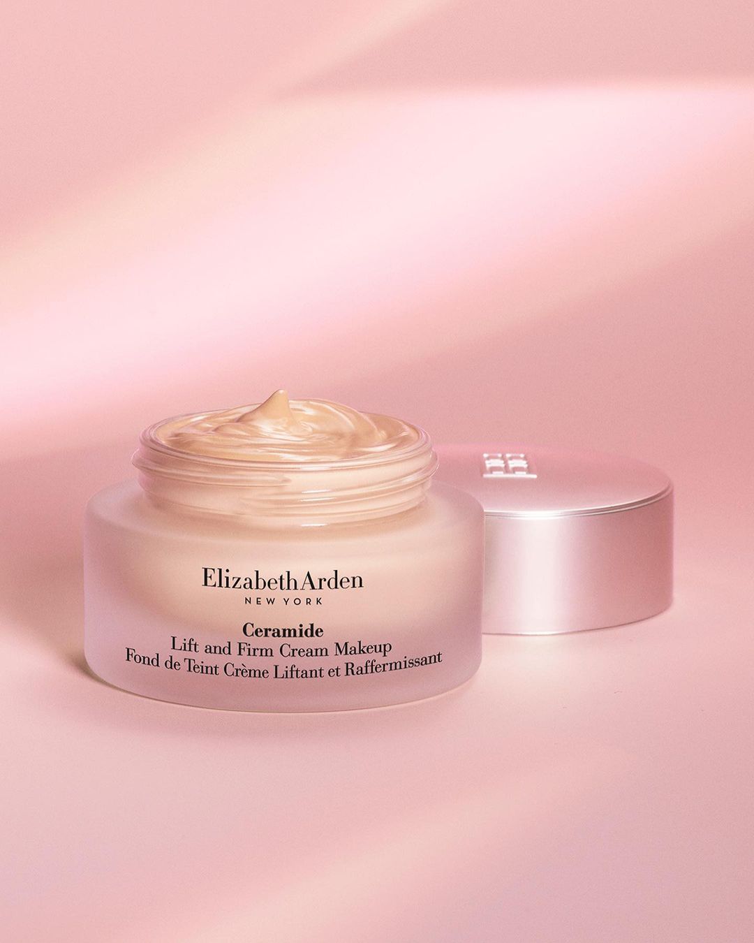 Elizabeth Arden Ceramide Lift and Firm Cream Makeup jar with product shown on a pink backdrop with the lid to the right.