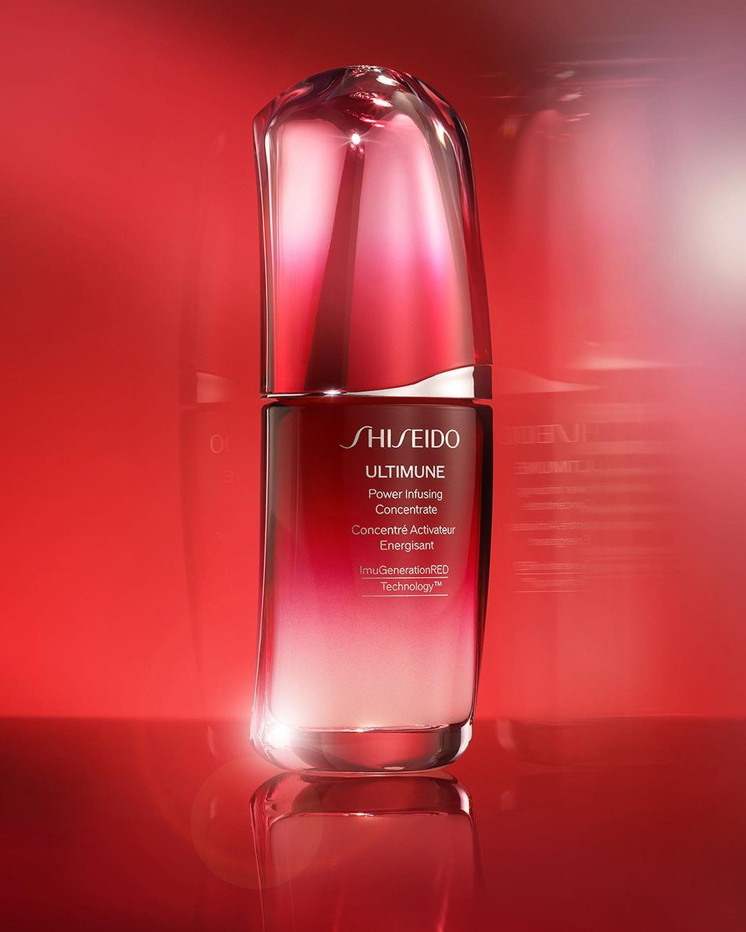 Shiseido Ultimune serum in a glossy red bottle on a reflective surface against a red background, showcasing beauty product.