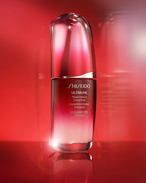 Shiseido Ultimune serum in a glossy red bottle on a reflective surface against a red background, showcasing beauty product.