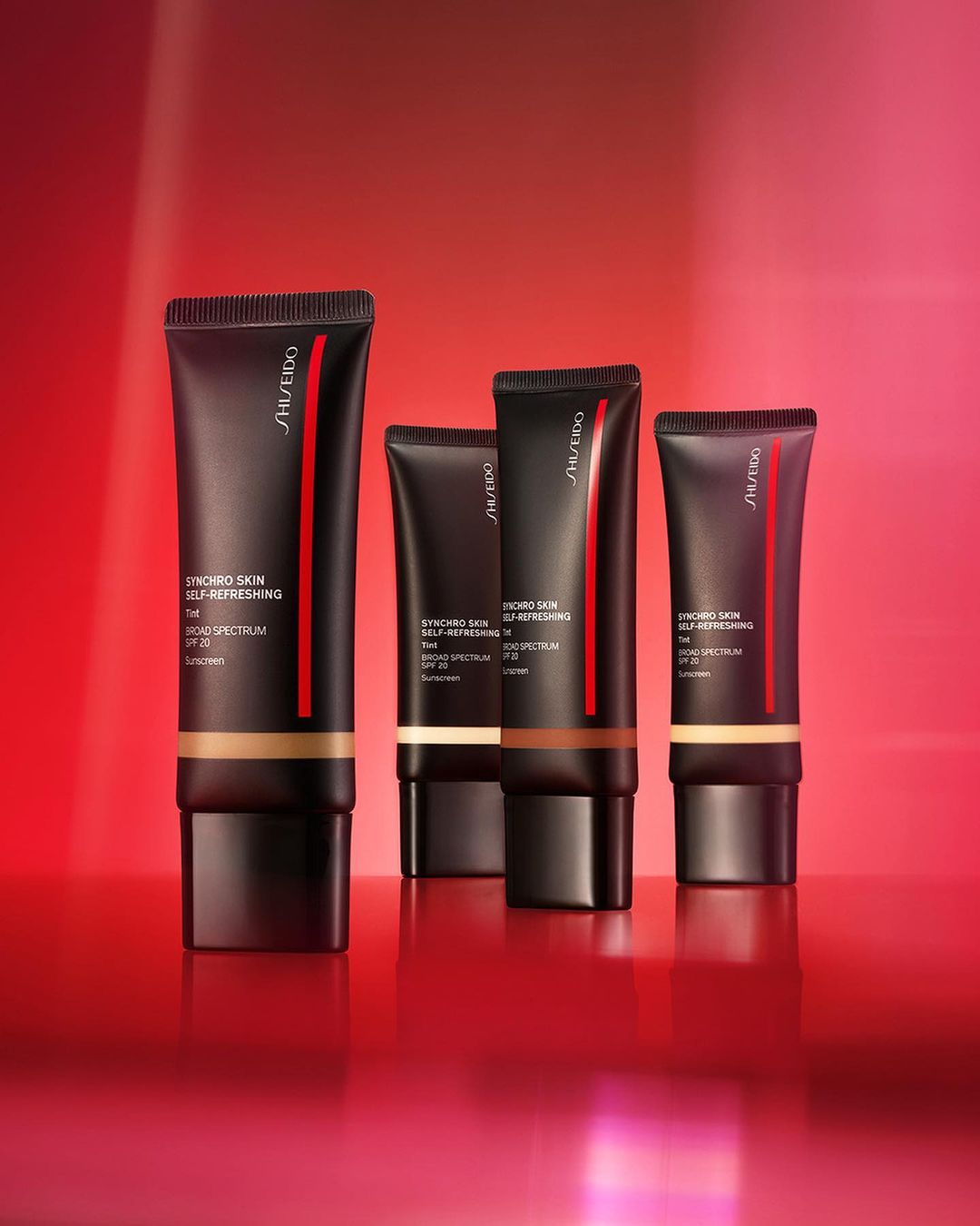 Studio shot of Shiseido Synchro Skin Self-Refreshing foundation bottles in various shades on a reflective red surface.