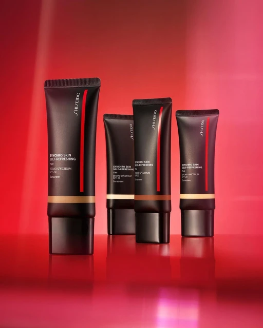 Studio shot of Shiseido Synchro Skin Self-Refreshing foundation bottles in various shades on a reflective red surface.