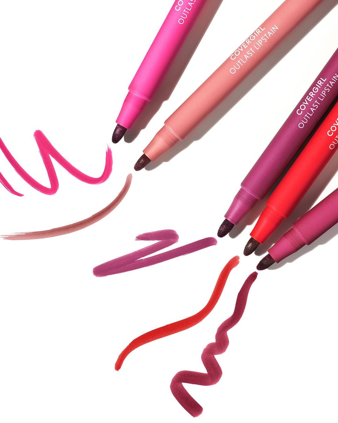 Close-up studio shot featuring an arrangement of colorful Covergirl Outlast Lipstain markers against a white backdrop with vibrant swatches.