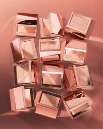 Flat lay photograph of multiple rose gold makeup compacts arranged neatly on a warm monochromatic pink surface.