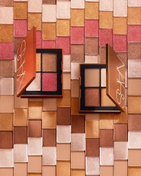 Two open NARS eyeshadow palettes displayed flat against a tiled background of shimmering bronze, gold, and pink squares.