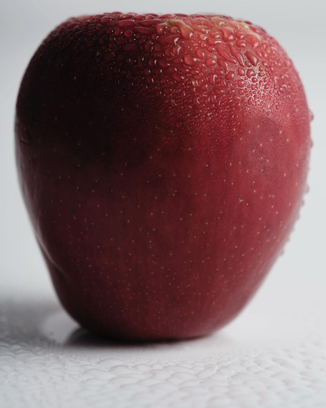 Close-up shot of a shiny, vibrant red apple with water droplets on its skin, set against a clean white background.