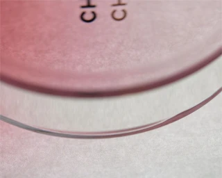 Close-up macro shot of a pink translucent cosmetic container resting on a textured white paper surface