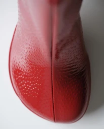 Close-up of a glossy red patent leather boot toe against a clean white background