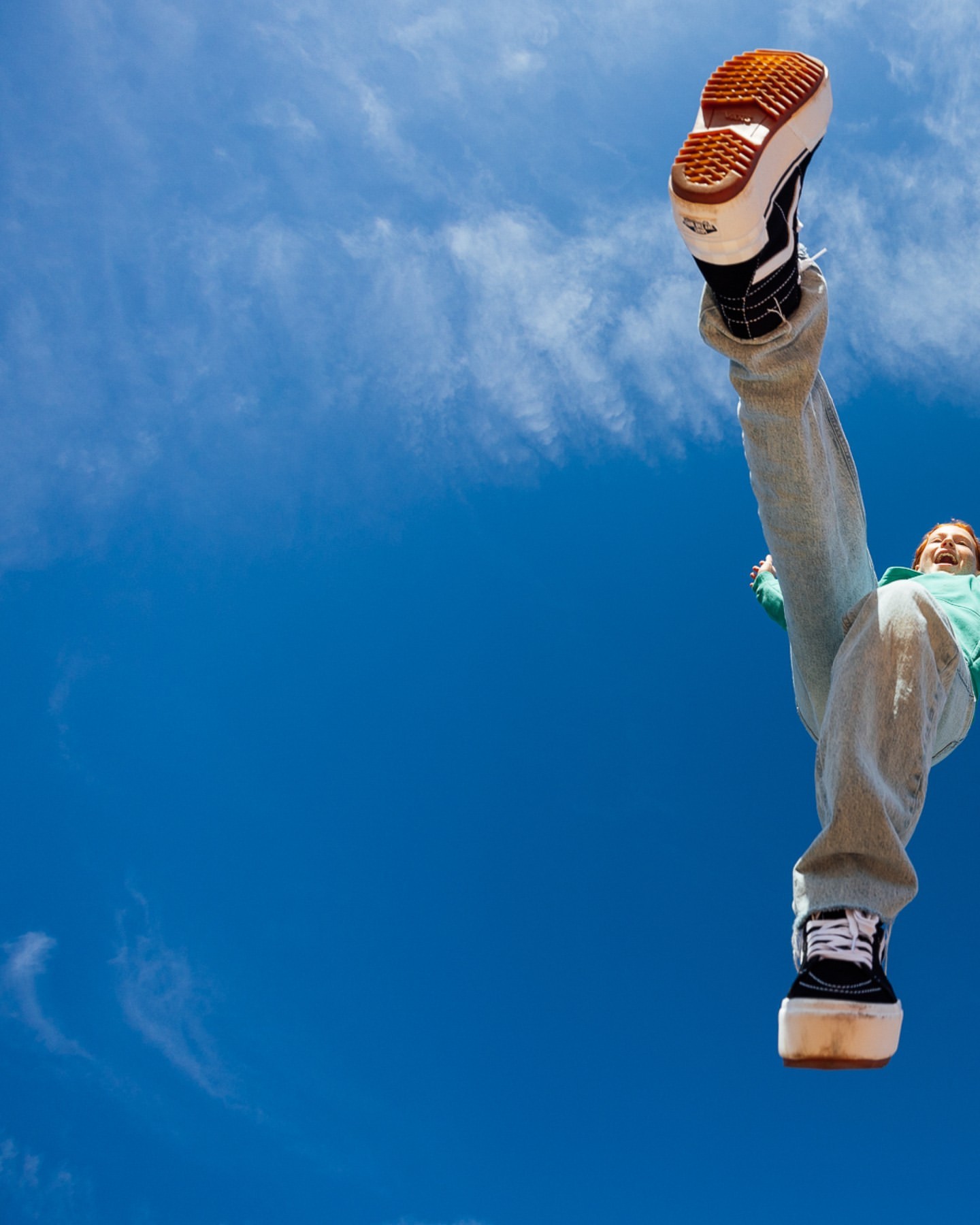 A young adult stands against a vibrant blue sky wearing platform shoes, capturing a unique perspective from below.