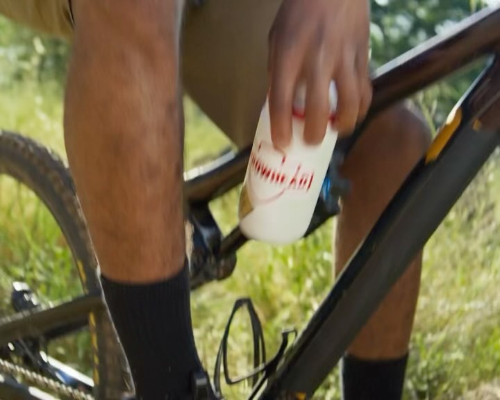 Close-up of a person on a mountain bike holding a white water bottle, showcasing sport and outdoor recreation.