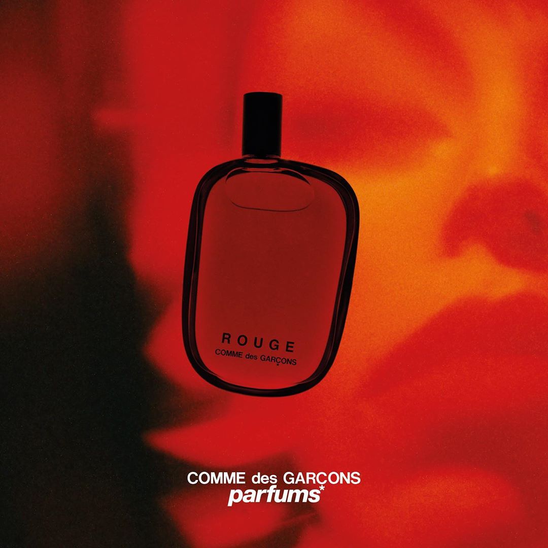 Comme des Garçons Rouge fragrance bottle on a red and orange gradient background, showcasing modern perfume design and branding.