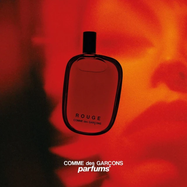 Comme des Garçons Rouge fragrance bottle on a red and orange gradient background, showcasing modern perfume design and branding.