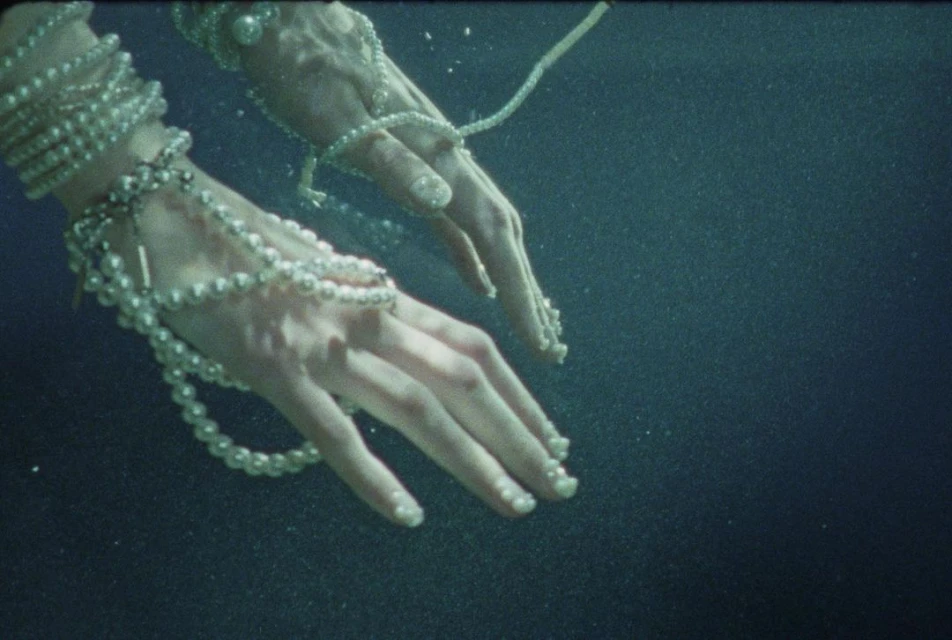 Elegant hands adorned with pearl jewellery submerged underwater in a serene, dark blue environment, capturing a moment of ethereal beauty.