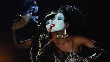 Two women with theatrical white face makeup and dark hair in theatrical cabaret attire posing against a dark background