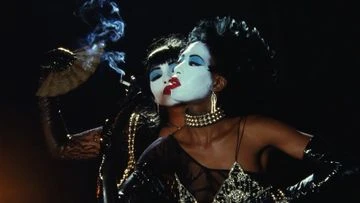 Two women with theatrical white face makeup and dark hair in theatrical cabaret attire posing against a dark background