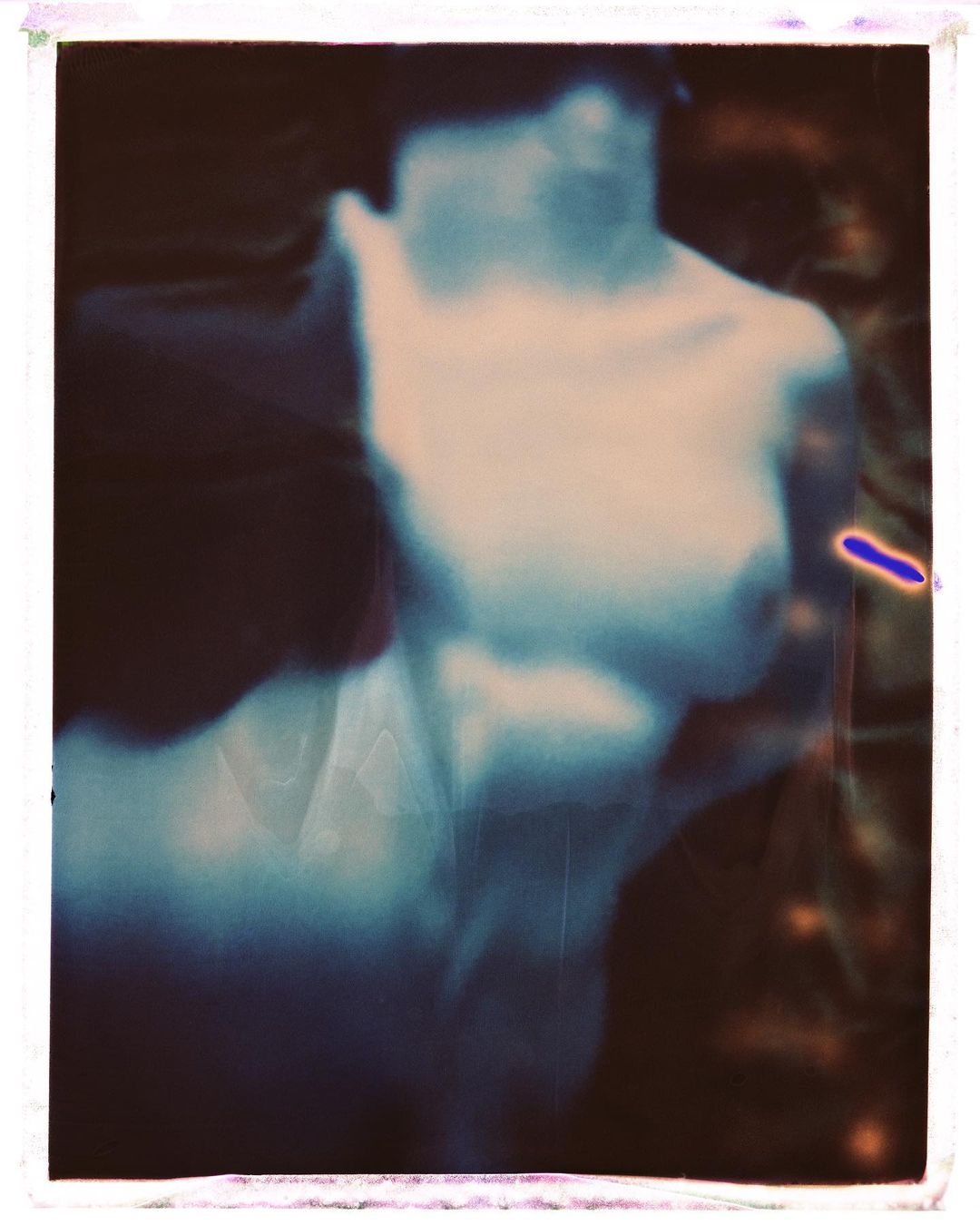 Figure study of a pale, blurred adult with the chest and torso visible, against a dark background with white border, in indoor setting.