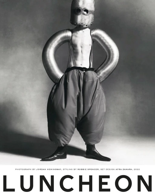 Artistic black and white studio portrait of a person with metallic headgear and tubing, paired with oversized trousers and boots.