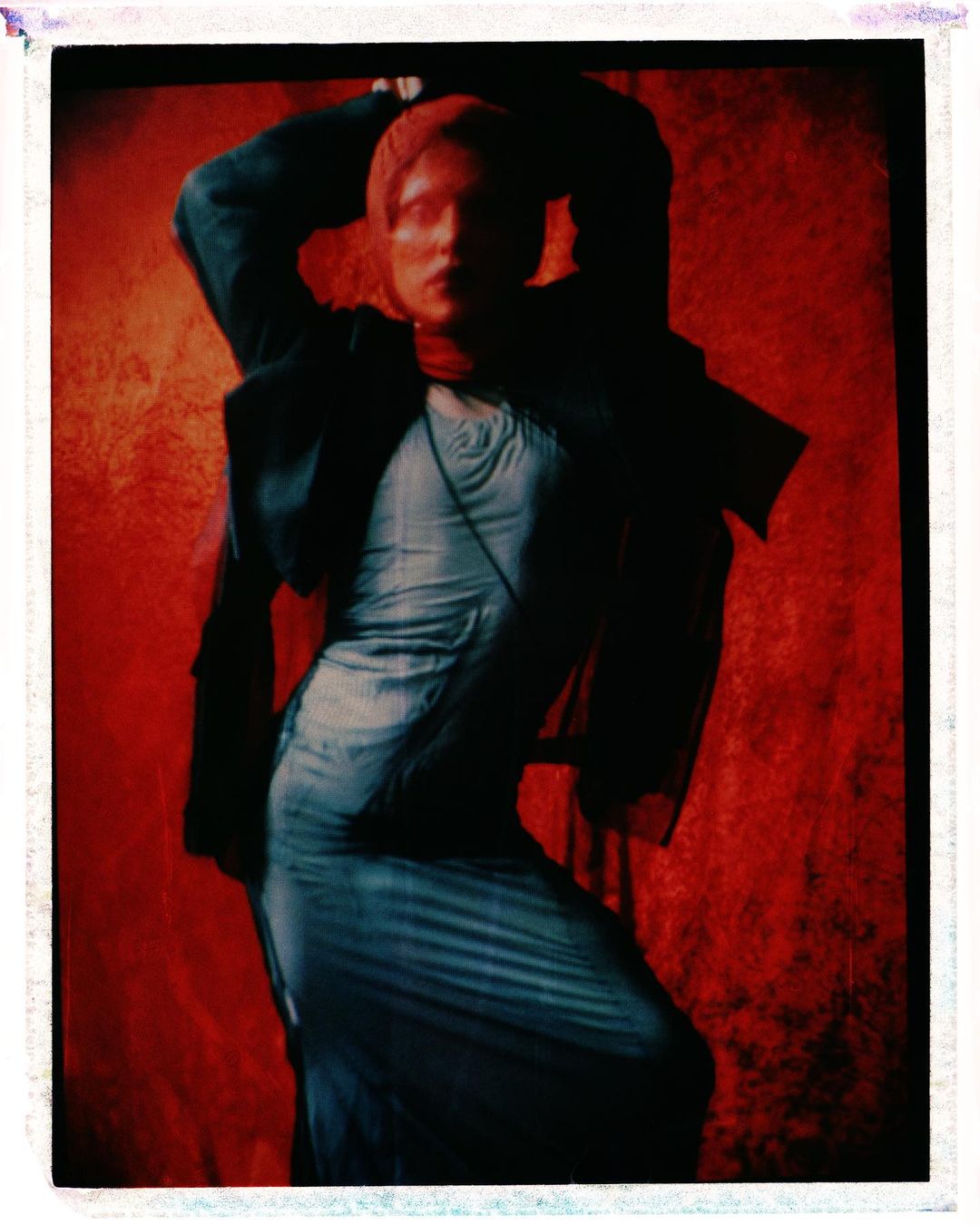 Model in a blue dress and dark jacket posing against a red textured backdrop by Jordan Hemingway