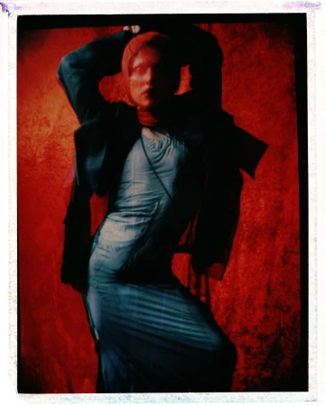 Model in a blue dress and dark jacket posing against a red textured backdrop by Jordan Hemingway
