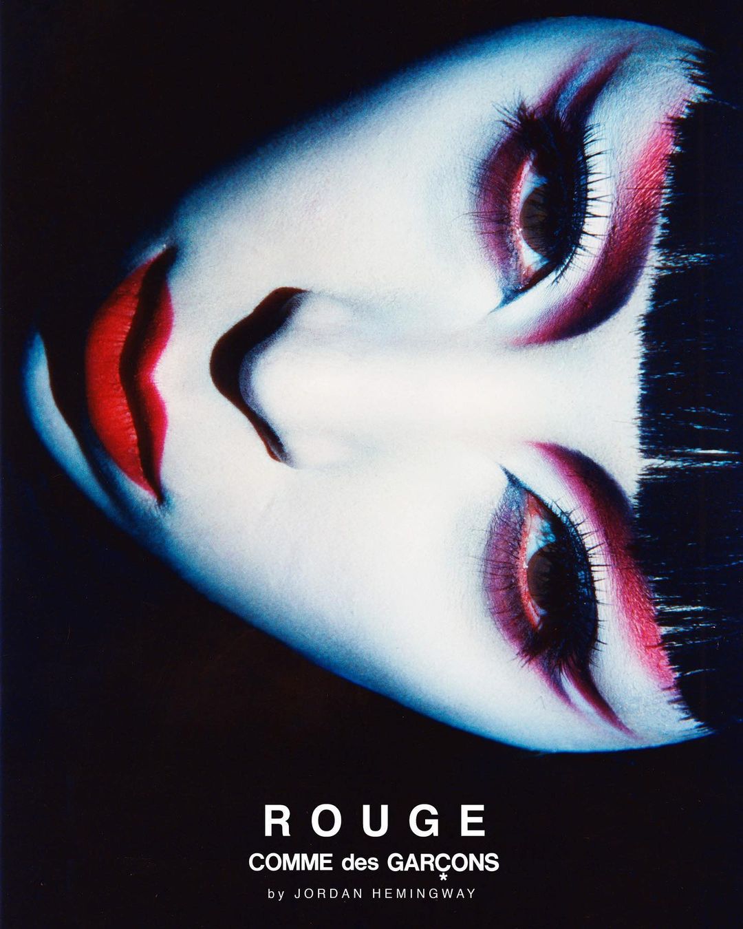 Dramatic close-up portrait of a woman with bold red makeup and dark hair against a black background, beauty and cosmetics focus.