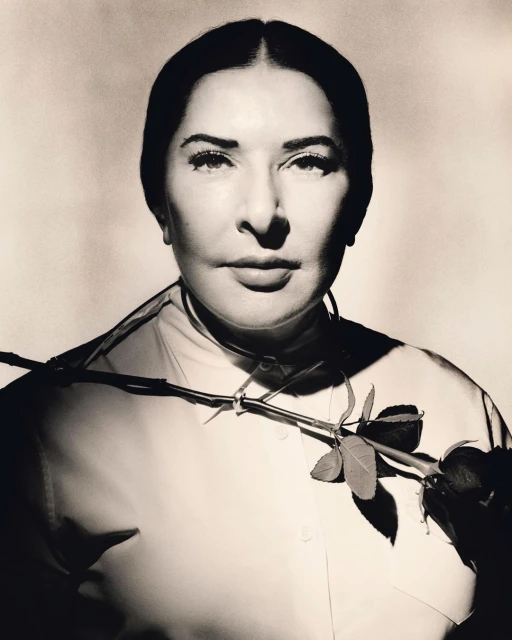 Monochrome portrait of an adult woman with dark hair wearing a collared shirt, adorned with a rose stem across her chest in studio lighting.