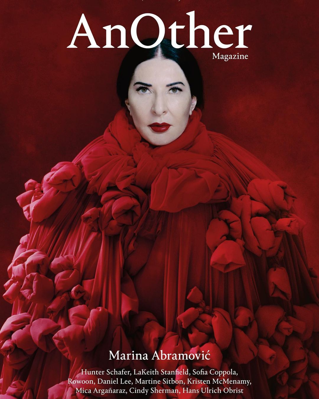 Close-up magazine cover shot of Marina Abramović wearing a red tulle garment with gathered floral adornments over a red background.