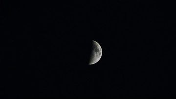 Close-up of a half-illuminated moon against a dark night sky. The moon's surface shows detailed craters and textures.