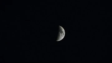 Close-up of a half-illuminated moon against a dark night sky. The moon's surface shows detailed craters and textures.