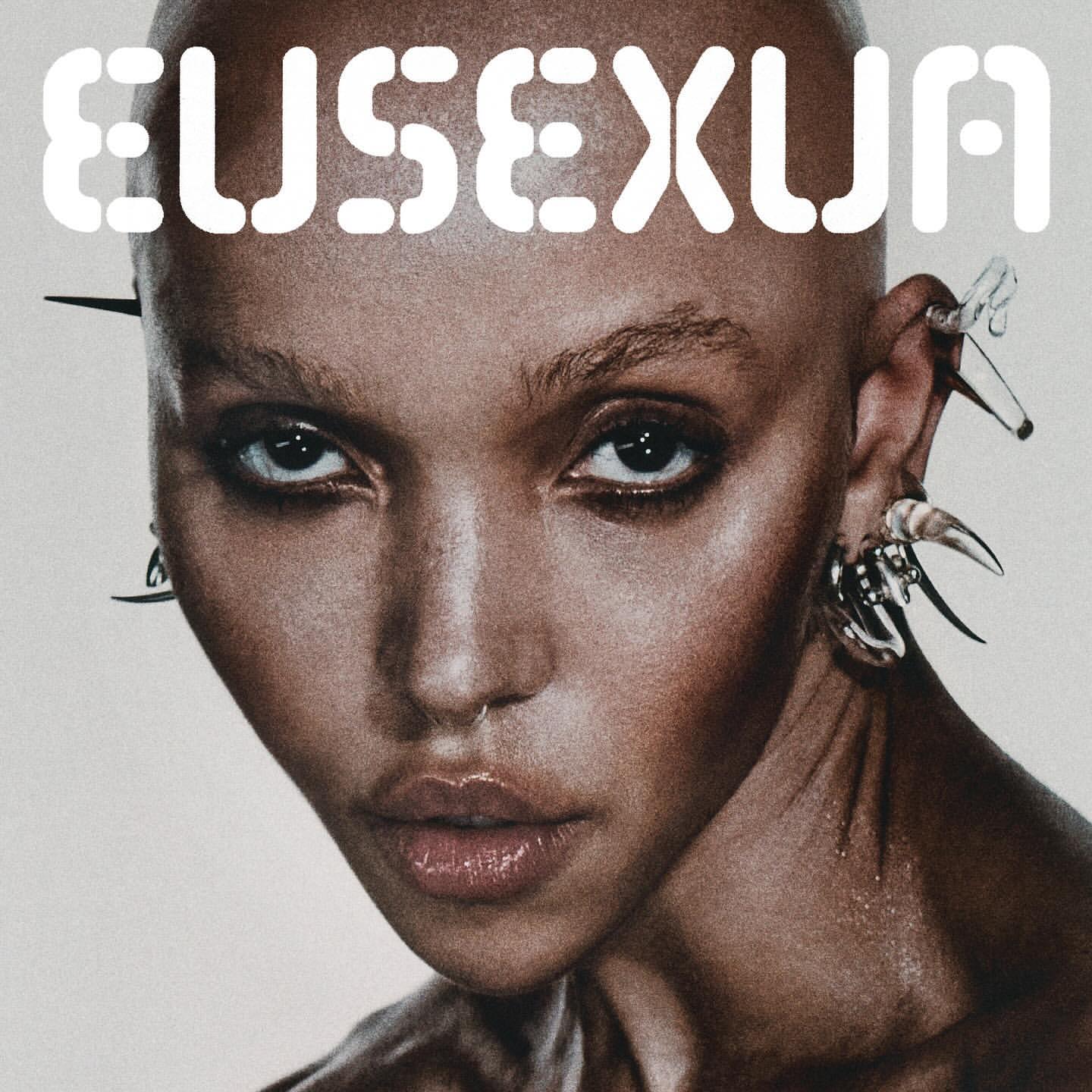 Close-up portrait of a bald woman with clear spike earrings, a nose ring, and large text reading 'EUSEXUA' across the top.