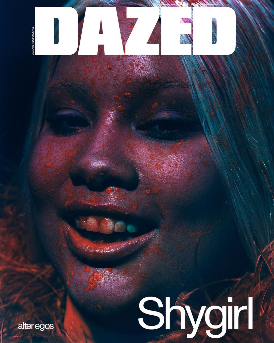 Close-up portrait of a woman with light-colored hair and reddish cosmetic splashes, featured on the cover of Dazed magazine.