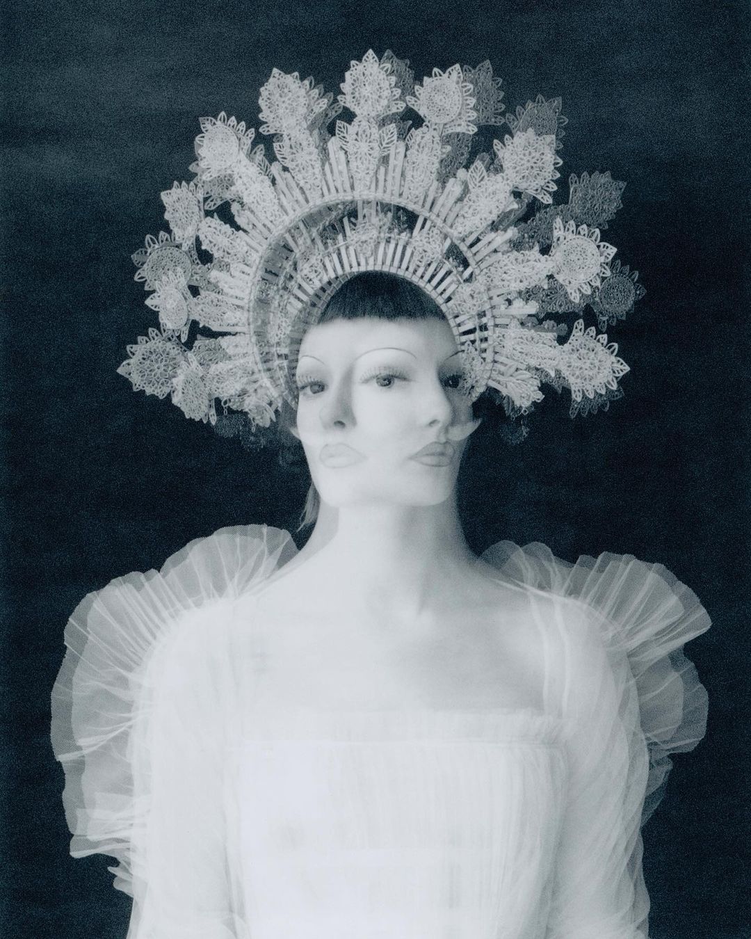 Ghostly photographic portrait of a woman with multiple faces wearing a white lace dress and ornate headpiece against a dark background.