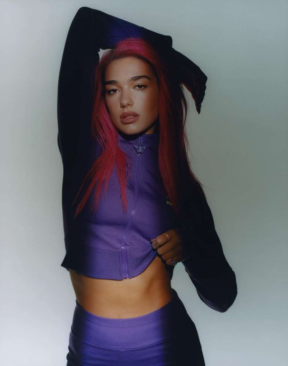 Fashionable woman with pink hair posing in purple athletic wear against a neutral backdrop, creating a vibrant and modern aesthetic.