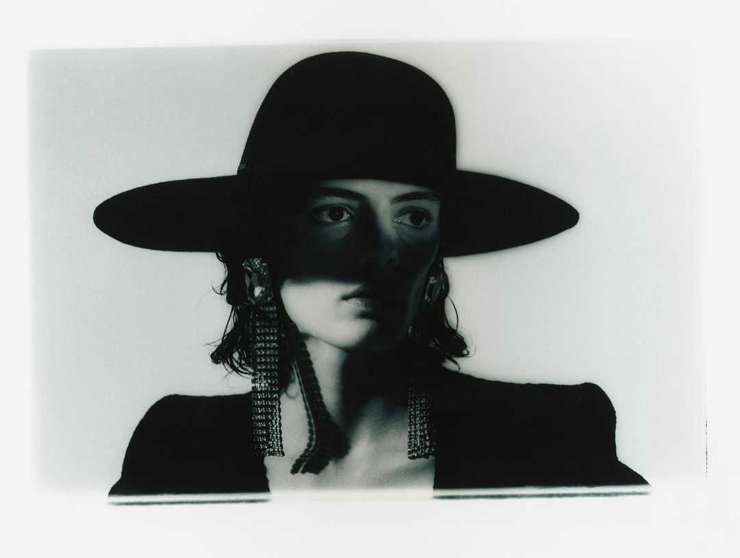 Model in a wide-brim black hat and sparkling fringe earrings with dramatic shadows across the face by photographer Jordan Hemingway