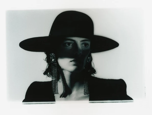 Model in a wide-brim black hat and sparkling fringe earrings with dramatic shadows across the face by photographer Jordan Hemingway