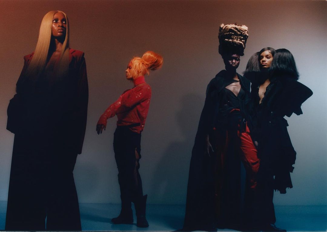 Fashion editorial shot of five diverse women in dramatic couture against a gradient backdrop with dynamic lighting, posing in various stylized looks.