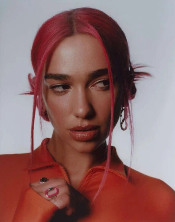 Portrait of a woman with vibrant pink hair wearing an orange top against a neutral light background