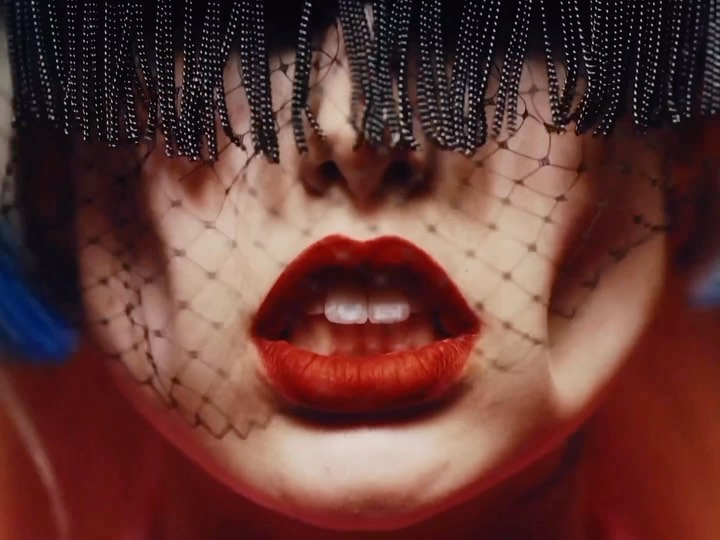 Close-up of woman's face with red lips, adorned with a netted veil and beaded fringe, creating a dramatic beauty and fashion statement.