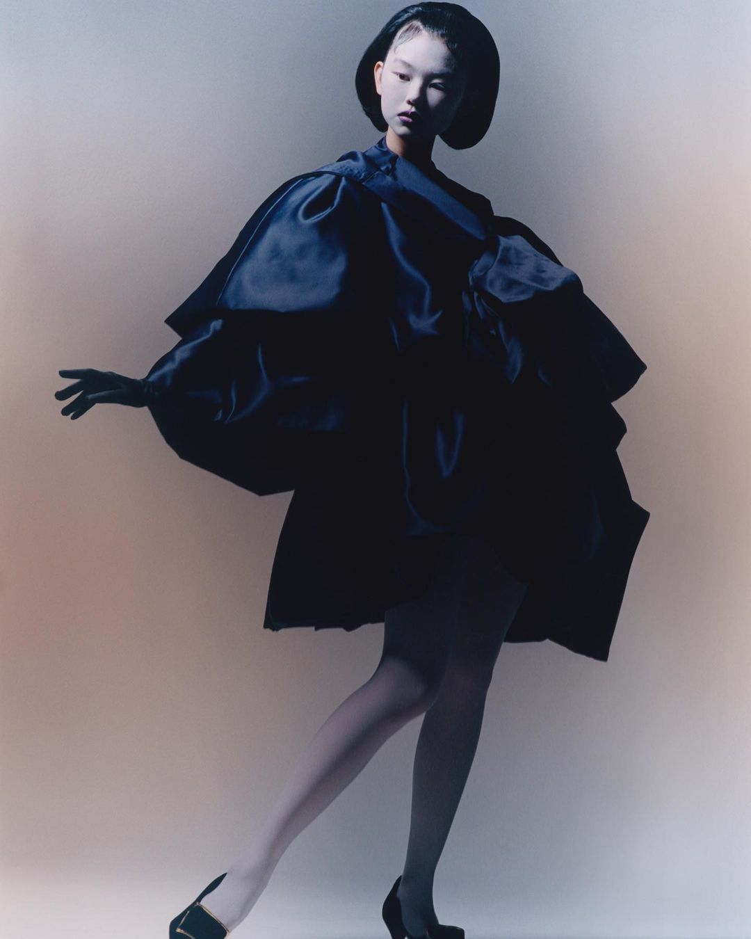 Model wearing voluminous black satin dress and sculptural hat photographed by Jordan Hemingway