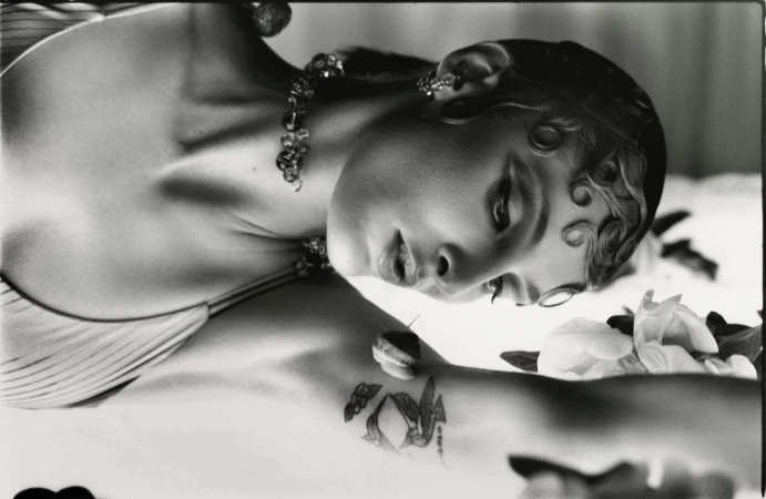 Black and white portrait of a woman with sculpted baby hair, beaded necklace, and a small snail on her tattooed arm by Jordan Hemingway