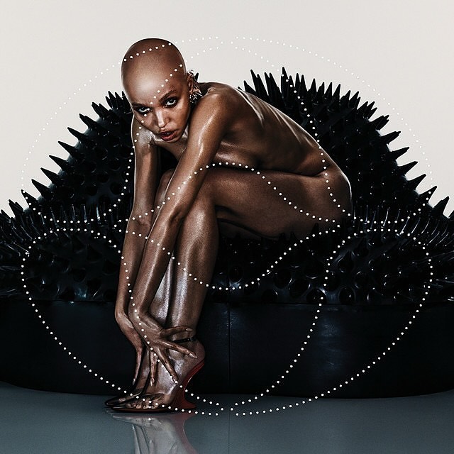 Striking art photo features a posed, bald adult woman with bronze skin seated on a black spiked surface with a dotted overlay.