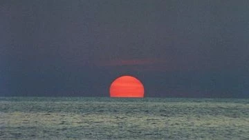Dramatic sunset over the ocean, featuring a vivid orange sun partially submerged on the water horizon, creating a peaceful and serene scene.