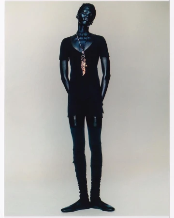 Model in black clothing wearing layered pendant necklaces against a neutral seamless backdrop