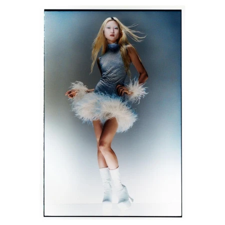 Full-length portrait of a young woman with blonde hair, wearing a blue mini dress with feathered hem and white platform boots in studio lighting.