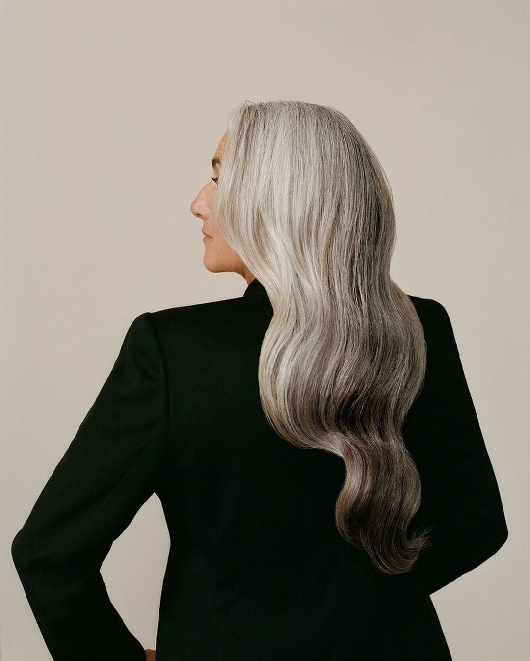 Profile of an elderly woman with gray hair wearing a black jacket against a neutral backdrop in a beauty and fashion portrait.