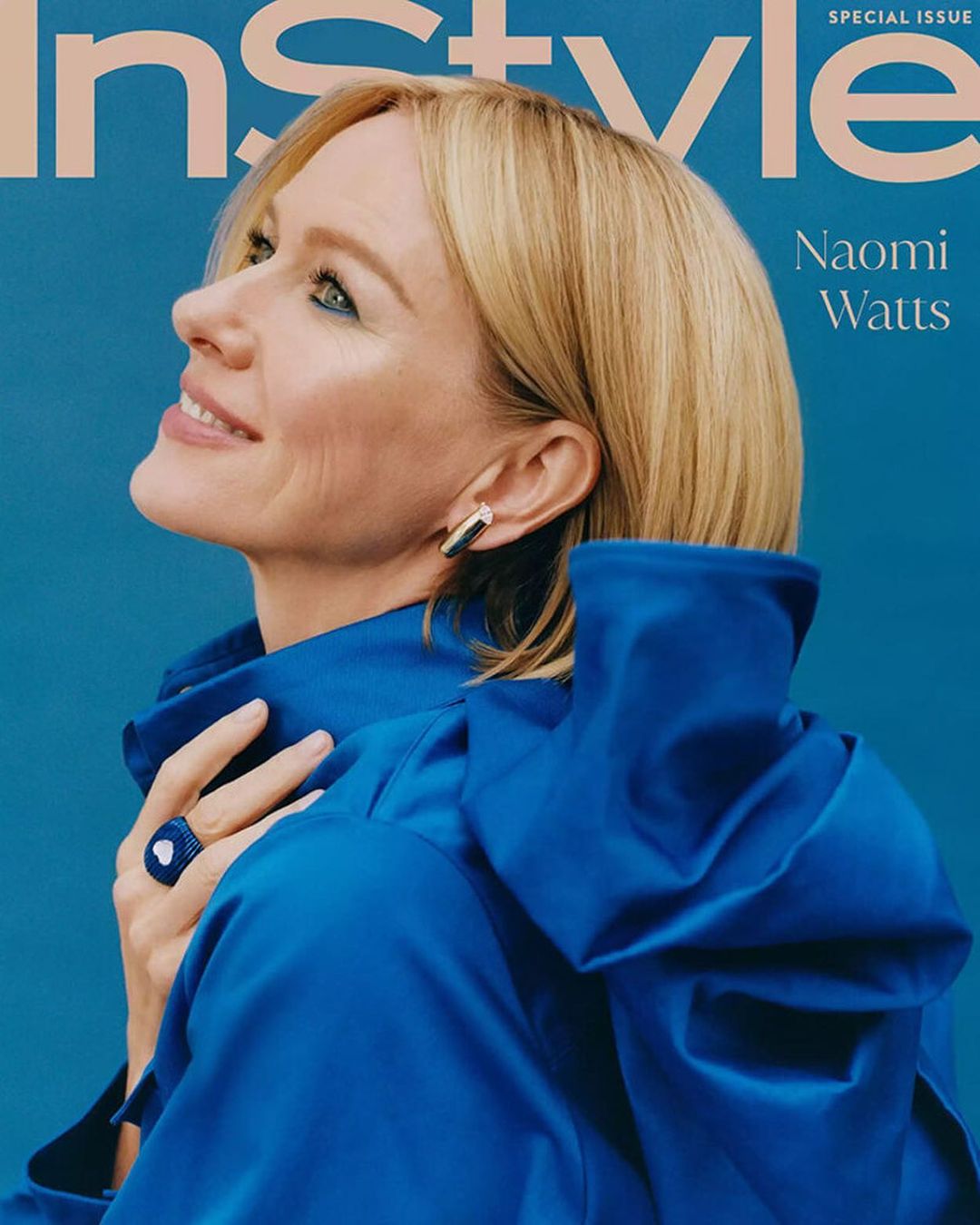 Naomi Watts on magazine cover wearing a blue dress and ring, smiling and looking up against a blue background with magazine text.