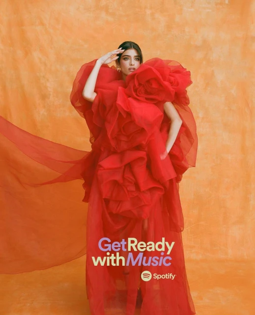 Young woman in extravagant red ruffled gown strikes a pose against an orange textured backdrop in a fashion editorial style image.