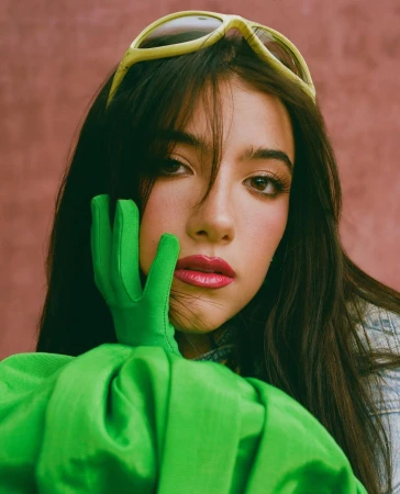 Close-up portrait of a woman wearing bright green gloves, a vivid green top, and yellow sunglasses resting on her dark hair.