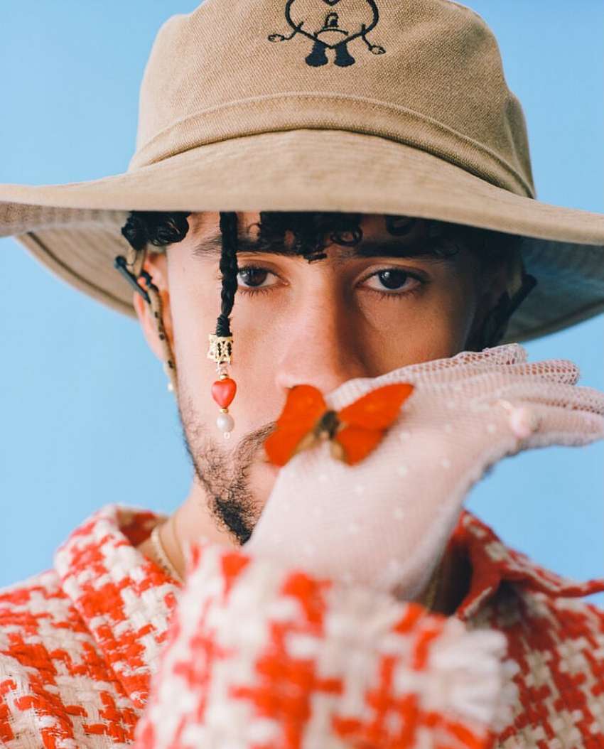 Portrait of a man wearing a hat and red patterned jacket posing in front of a blue background with a red butterfly on his glove.
