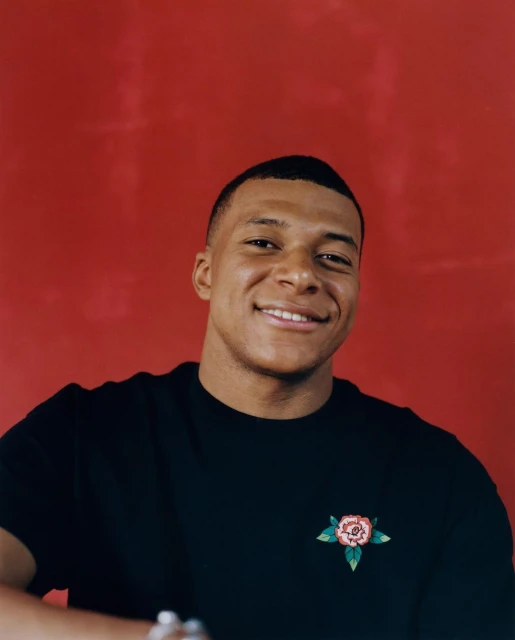 Portrait of a smiling adult male with short hair wearing a black t-shirt with a rose design against a solid red backdrop.