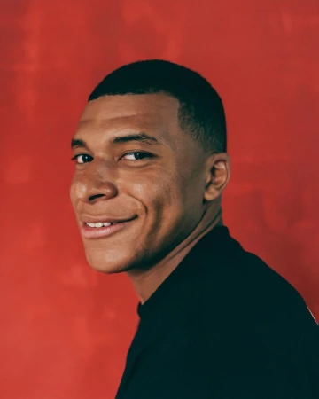 Portrait of Kylian Mbappe smiling slightly against a textured red background, photographed by Josefina Santos.