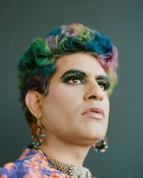 Portrait of a person with multicolored hair, dark eye makeup, nose ring, beaded hoop earrings, and a metallic choker by Josefina Santos.
